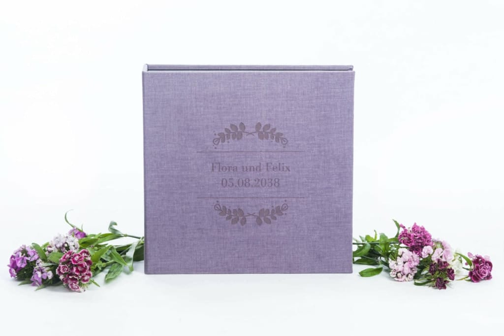 Elegante Hochzeitsalbum in lila Stoff mit personalisiertem Gravurtext, umgeben von purple Blumen, perfekte Hochzeitsfotografie- und Erinnerungsfoto-Requisiten.