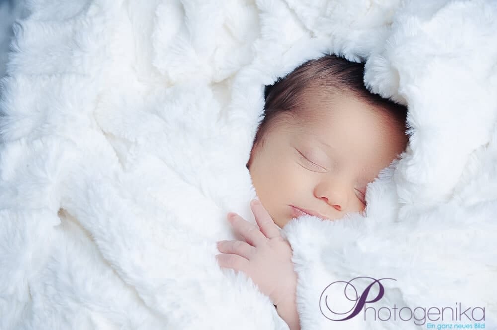 Gentle newborn photo in Munich, baby in a soft, white fur coat, professional baby photography at Photogenika photo studio in Munich.