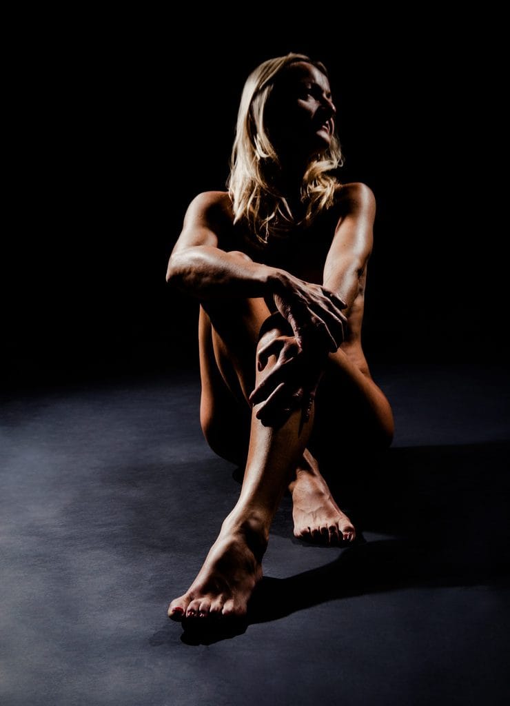 Colorful artistic nude portrait of a woman in a dark studio, professional photography, moody lighting, artistic nude photography for creative pictures in Munich.