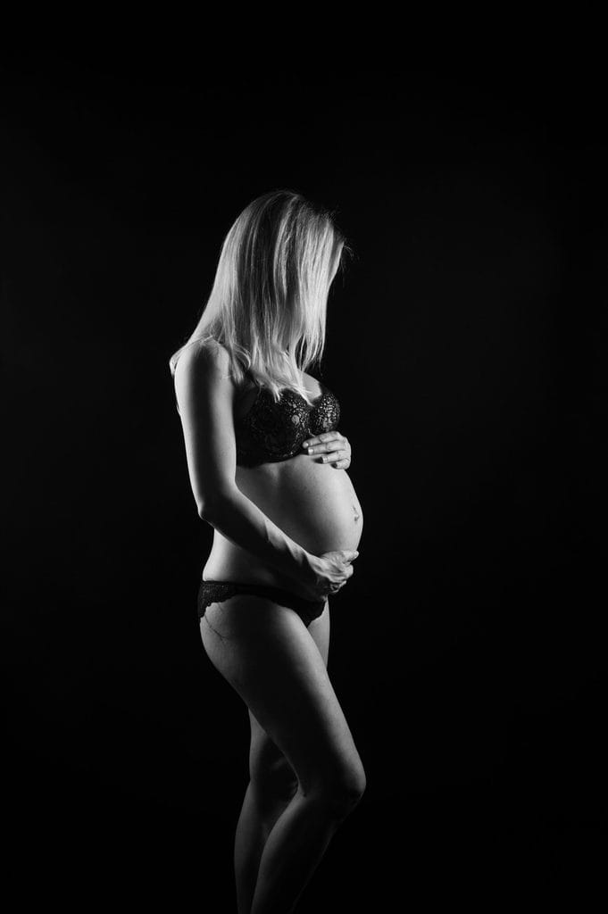 Porträt einer schwangeren Frau in schwarzer Unterwäsche, künstlerisch fotografiert in Schwarz-Weiß, aufnahmen von einem professionellen Fotostudio in München.