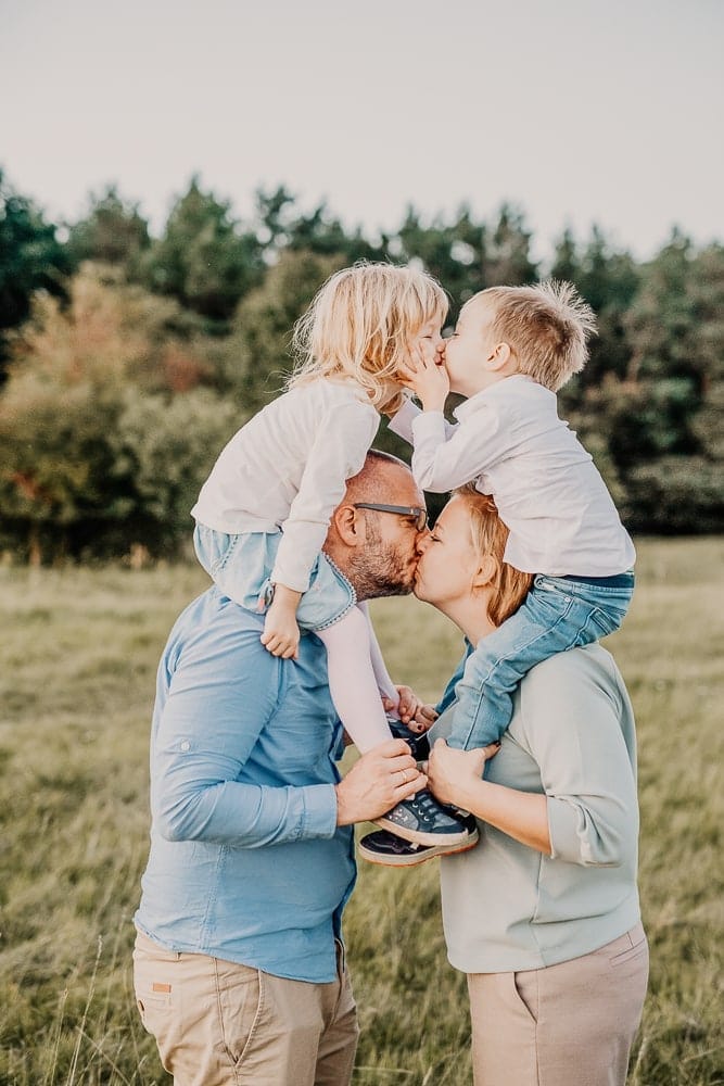 Familienfoto bei Photogenika Fotostudio in München, professionelles Fotoshooting im Freien mit Eltern und Kindern, natürliche Familienportraits, Kinder liebevoll einander küssend.