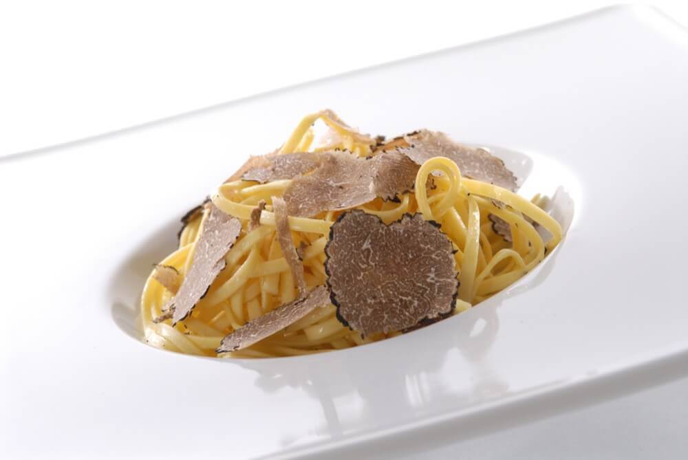Feines Pasta-Gericht mit Trüffelscheiben auf weißem Teller, kreative italienische Küche, hochwertige Zutaten, Kulinarik in München, elegantes Restaurantambiente, Gourmet-Genuss, Spezialitäten aus Italien, atmosphärisches Essen.
