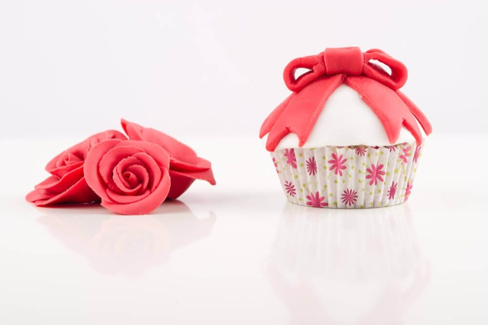 Bunte Cupcake-Deko mit rosa glitzernden Blüten aus Fondant, kreative Backkunst im Fotostudio.