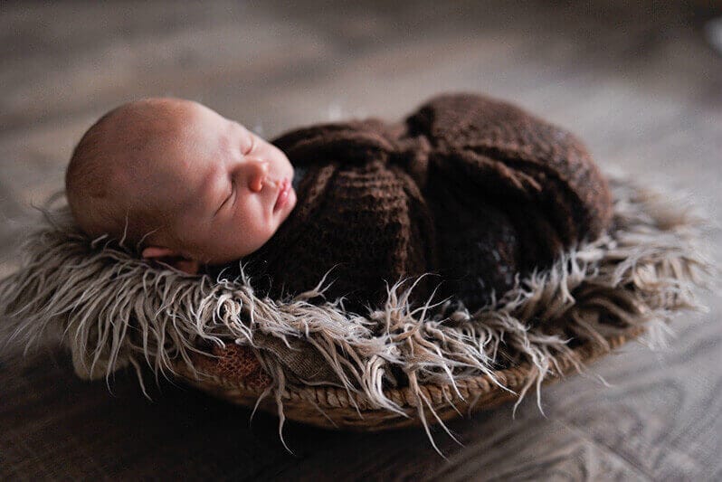 Babyfotografie München, Neugeborenes in warmem Kleid auf kuscheligem Nest, professionelle Babyfotostudios, Sanfte Babyfotos bei Photogenika Fotostudio, liebevolle Neugeborenenshootings in München.