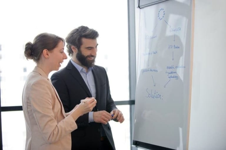 Businesswoman and businessman in a meeting in front of a whiteboard in a modern office in Munich.