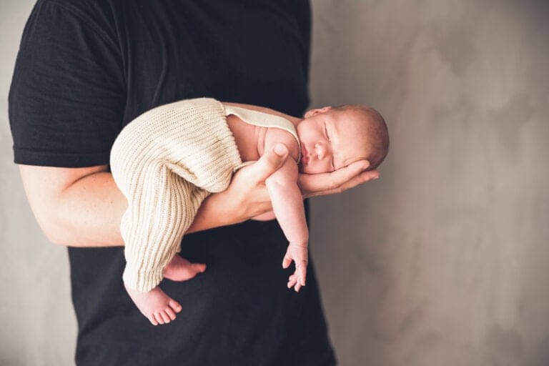 Delicate newborn baby in the arms of an adult, close-up, children's photography, loving baby shot, sweet infant in beige romper, warm photo shoot.