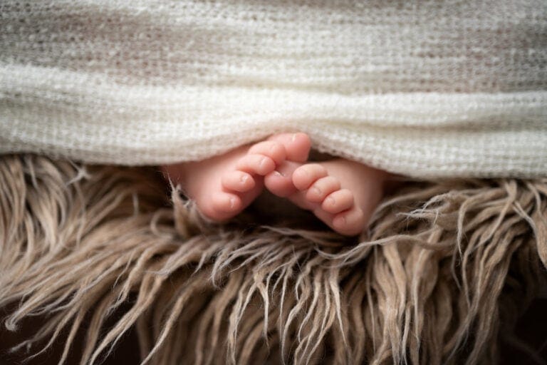 Delicate baby feet, closeup of tiny baby toes on soft fabric.