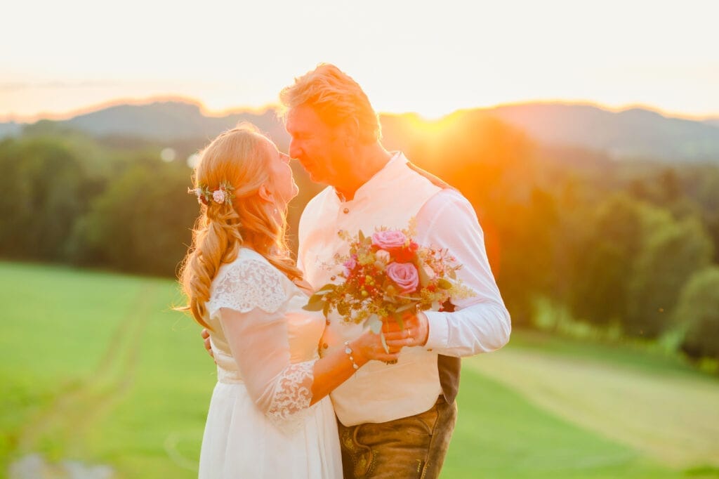 Liebespaar bei Sonnenuntergang, Hochzeitsfoto mit Blumenstrauß, romantisches Paarshooting im Freien, Naturkulisse, Emotionen, Hochzeitsfotografie, Hochzeit, Liebe