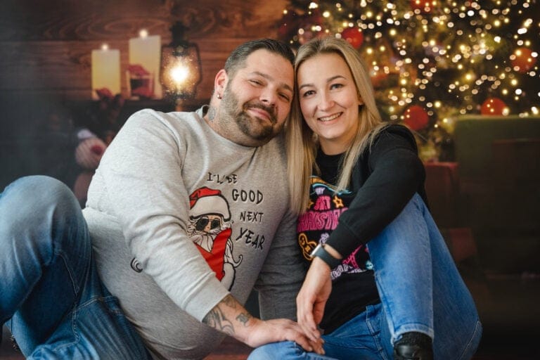 Fröhliches Paar bei Weihnachtsfeier, festliche Stimmung mit Weihnachtsbaum und Kerzen, gemütliches Ambiente.
