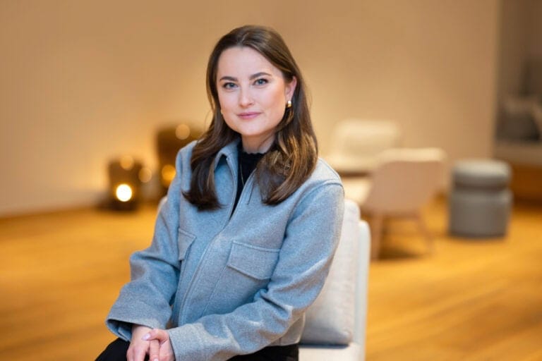 Stilvolle Frau im eleganten Blazer, modern und selbstbewusst, auf einer gemütlichen Sitzgelegenheit in einem eleganten Raum.