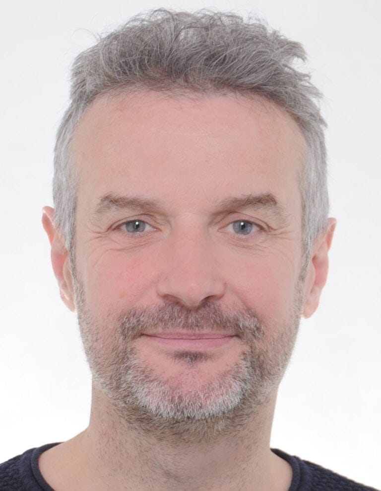 Passfoto eines Mannes mit grauem Bart und blauen Augen vor weißem Hintergrund.