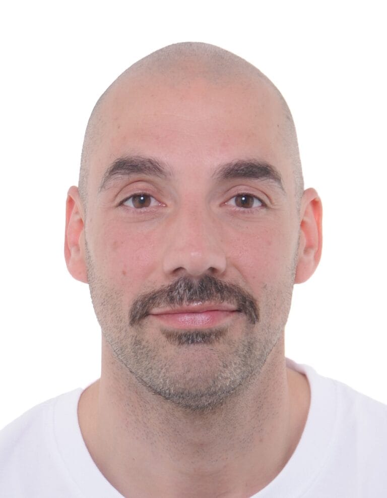 Passfoto eines Mannes mit Bart und Glatze, Nahaufnahme, freundlicher Gesichtsausdruck, professionelles Studiofoto.
