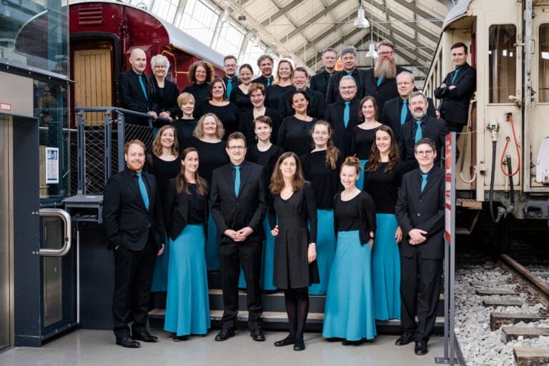 Gruppenfoto im Eisenbahnmuseum mit Chormitgliedern und Lokomotive, professionelle Porträtaufnahme, deutsche Museums- und Musikveranstaltung.