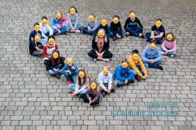 Fröhliche Grundschulklasse 4a im Schuljahr 2022/2023 auf gepflastertem Schulhof, lachende Kinder mit Emoji-Overlay.