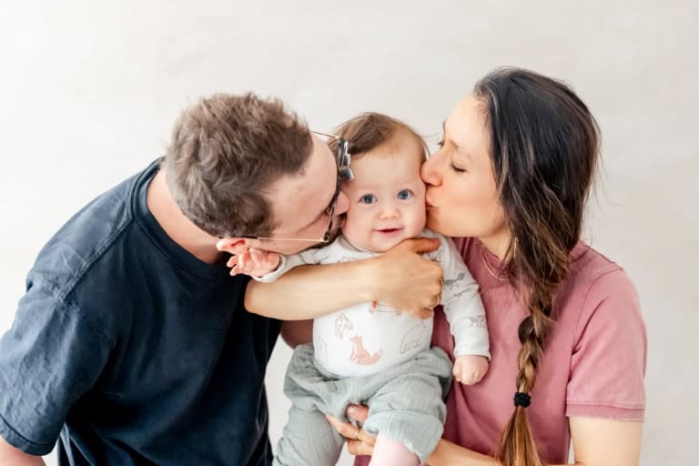 Familienfoto mit Eltern und Kleinkind, liebevolle Küsse, professionelle Kinder- und Familienshootings in München, emotionales Familienporträt, Baby in den Armen, natürliche Familienmomente.