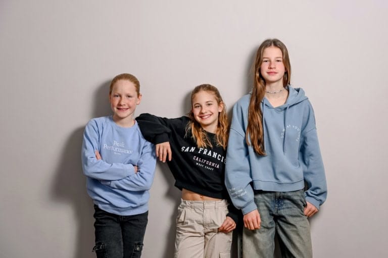 Fröhliche Jugendliche in Casual-Outfits posieren vor weißer Wand, lachend und entspannt, ideal für Familien-, Freizeit- oder Lifestyle-Fotografie in München.