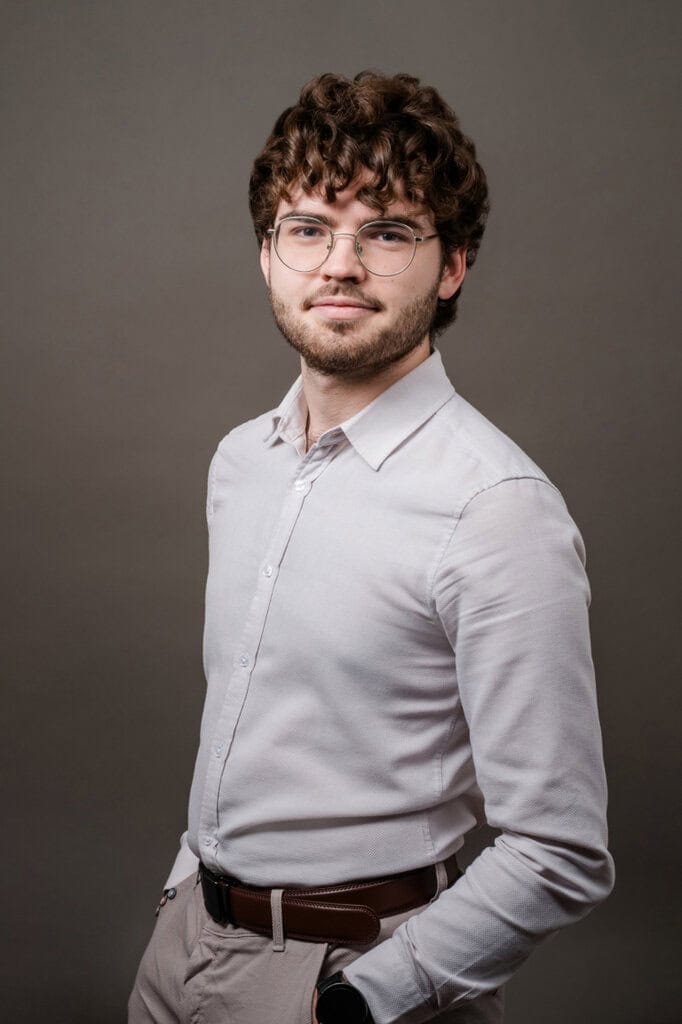 Junger Mann mit Brille und Locken im weißen Hemd für Bewerbung.