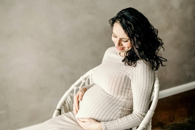 Schwangere sitzt entspannt im Korbsessel und blickt zum Bauch