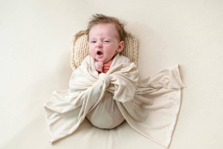 Cute baby pulls a face and yawns in a beige blanket