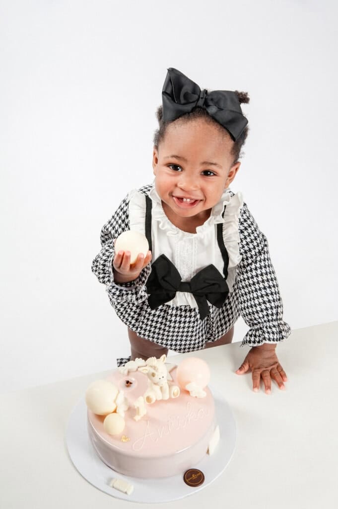 Glückliches Kind hält Tortendekoration beim Baby-Fotoshooting in die Kamera.