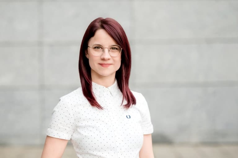 1. Junge Frau mit roten Haaren und Brille vor grauem Wandhintergrund, professionelles Portrait, hochwertige Fotografie.