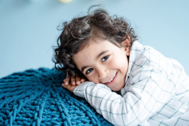 Ein Junge mit Locken liegt entspannt auf einem blauen Kissen.