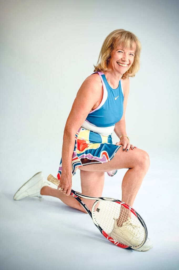 Aktive ältere Frau beim Tennisspielen, lachend, in sportlicher Kleidung, professionell fotografiert in einem hellen Studio.