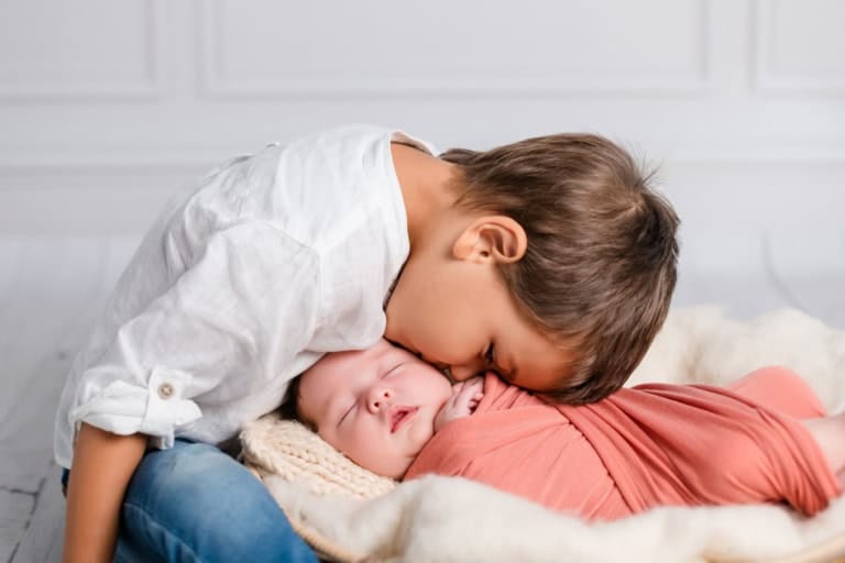 Big brother kisses the sleeping baby in the basket on the head