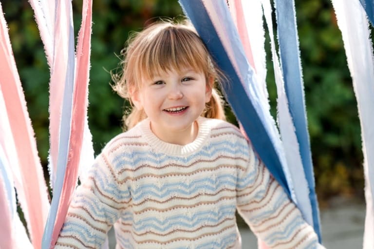 Ein fröhliches Kind schaut durch bunte Stoffbänder hindurch.