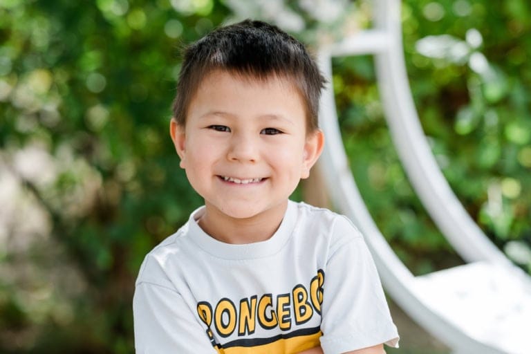 Porträt eines lächelnden Jungen vor grünem Hintergrund.