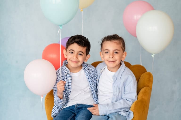 Zwei Jungen teilen sich einen Sessel inmitten bunter Luftballons.