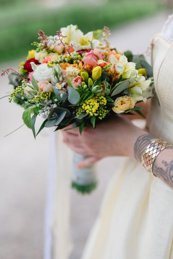 Farbenfroher Brautstrauß mit Rosen und Sommerblumen in der Hand.gehalten von einer Braut.