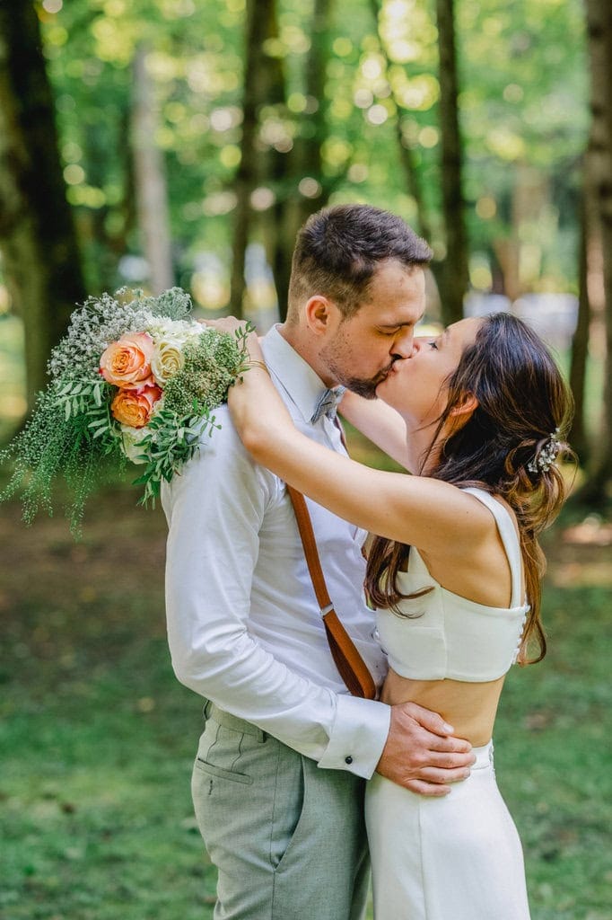Romantischer Kuss des Brautpaares bei einem Spaziergang im Wald.