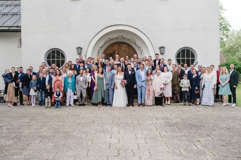 Großes Gruppenfoto der gesamten Hochzeitsgesellschaft vor der Kirche.